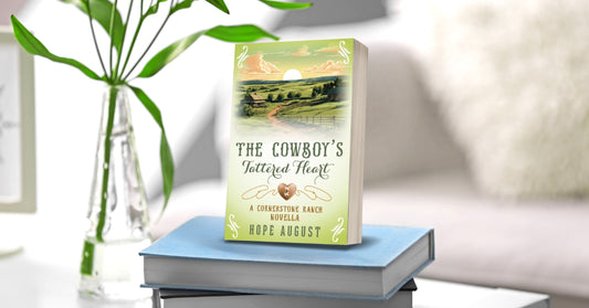 Book titled 'The Cowboy's Tattooed Heart' on a stack of books with a plant in the background